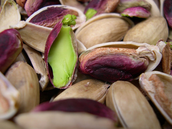 Dried pistachios in their shell, some open to show the violet-skinned seed