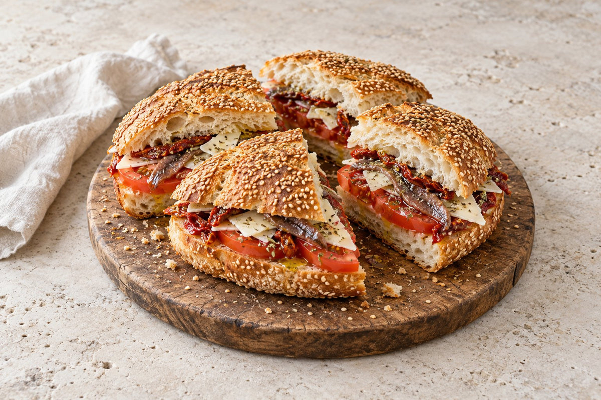 Pane cunzato: sesame bread filled with tomato, anchovies, sun-dried tomatoes and cheese, cut into quarters on a wooden board