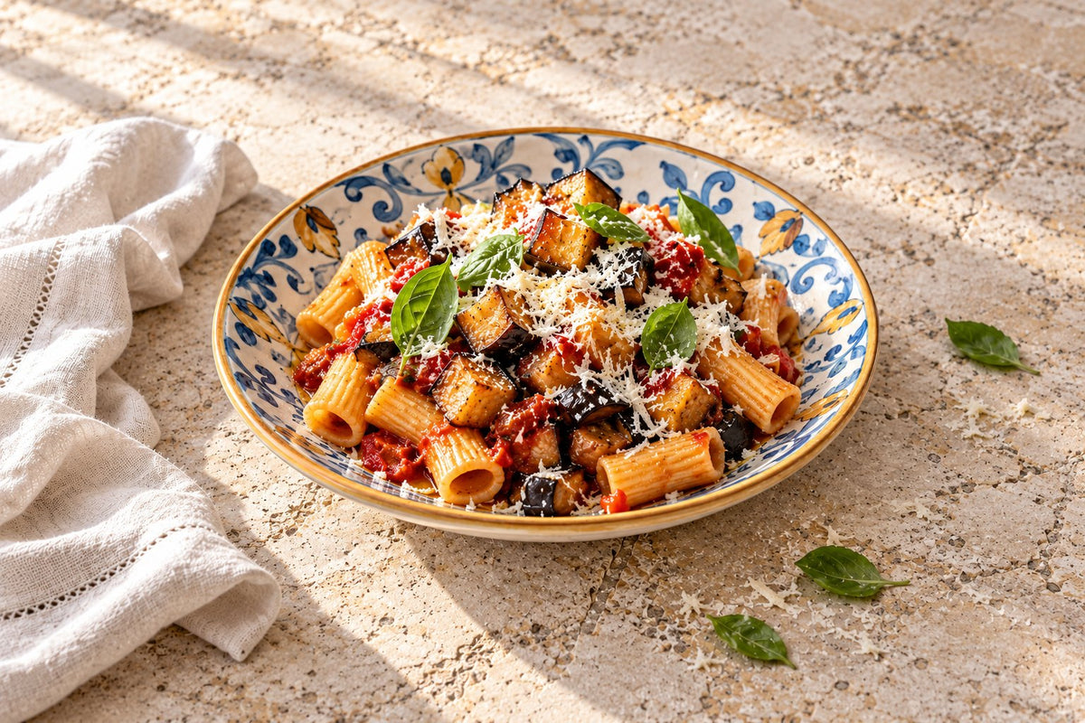 Rigatoni alla Norma with fried eggplant, tomato sauce, grated ricotta salata and basil in a blue and yellow Sicilian ceramic bowl