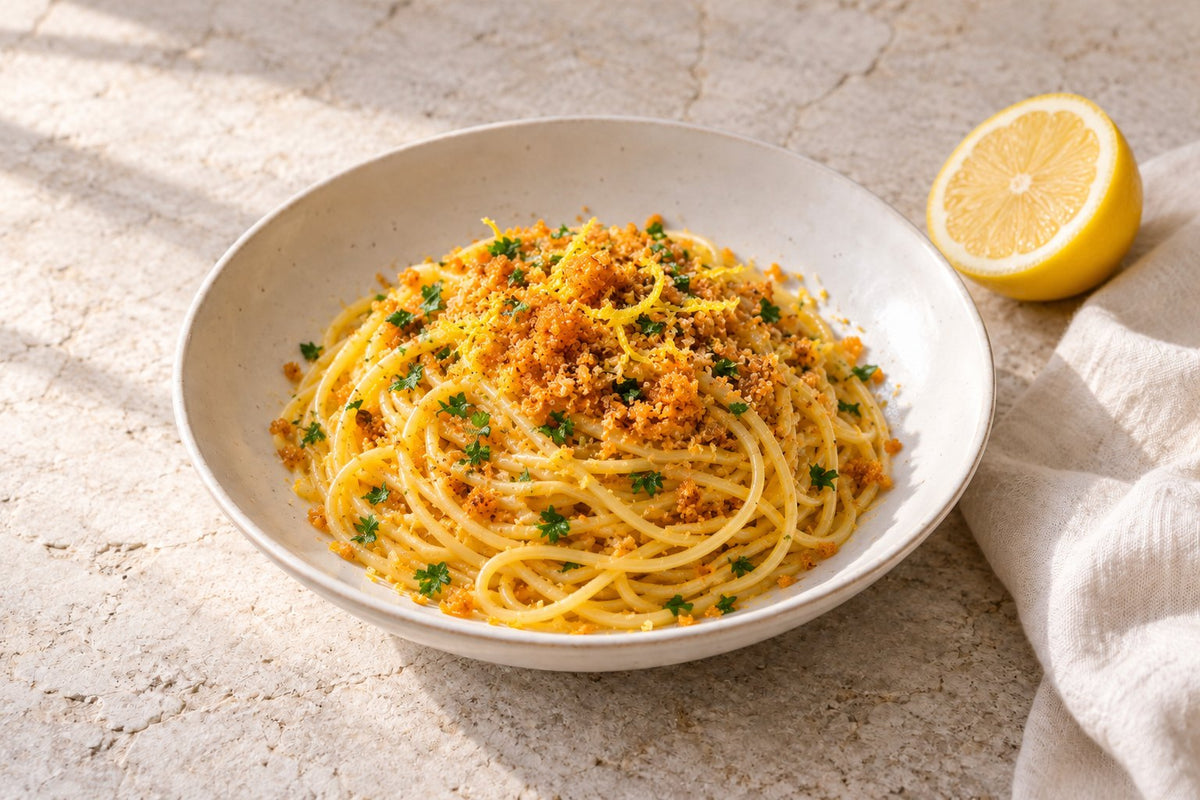 Spaghetti topped with grated tuna bottarga, lemon zest and parsley in a white bowl, half a lemon beside it