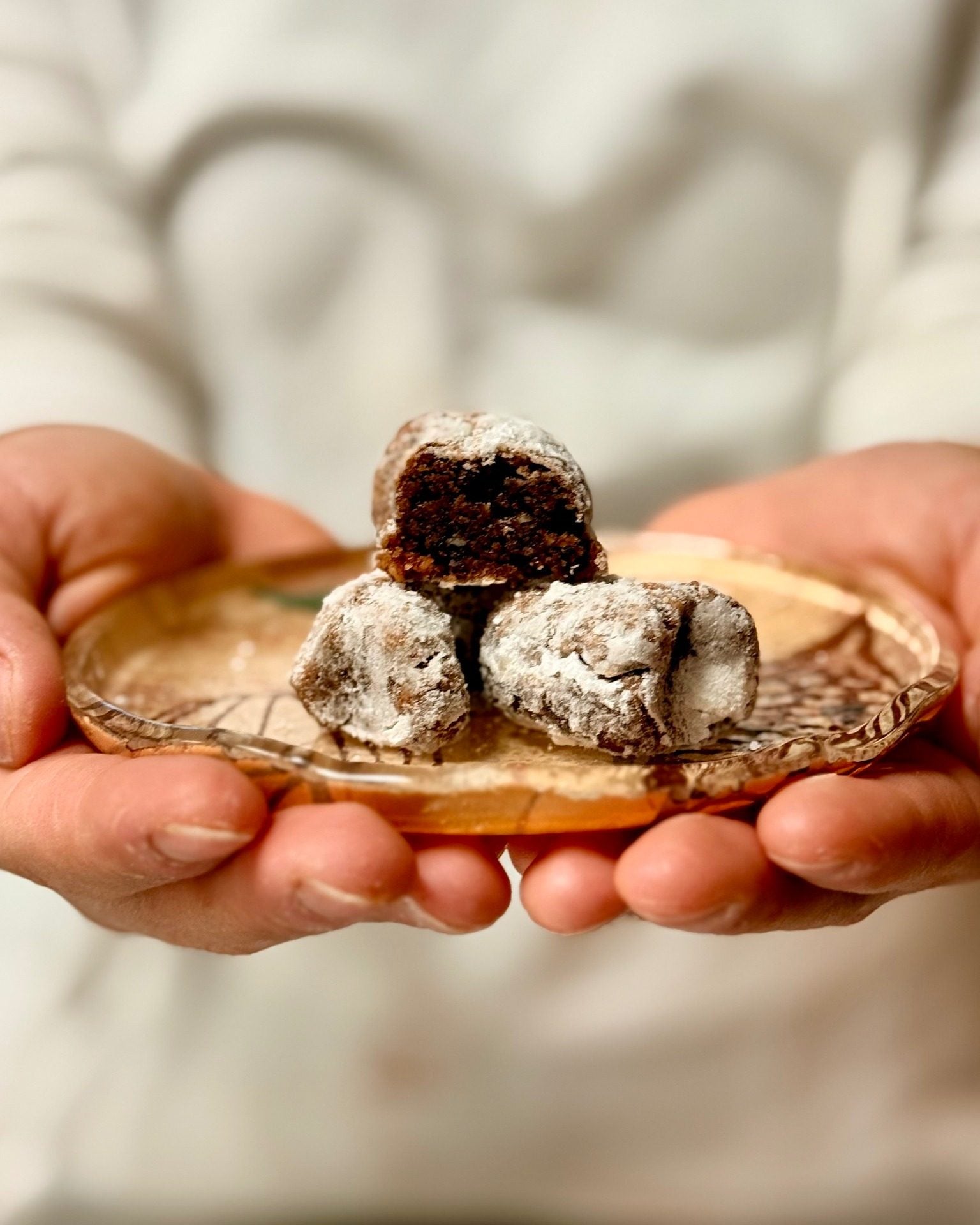 Chocolate sweets dusted with sugar offered on a small plate held in two hands
