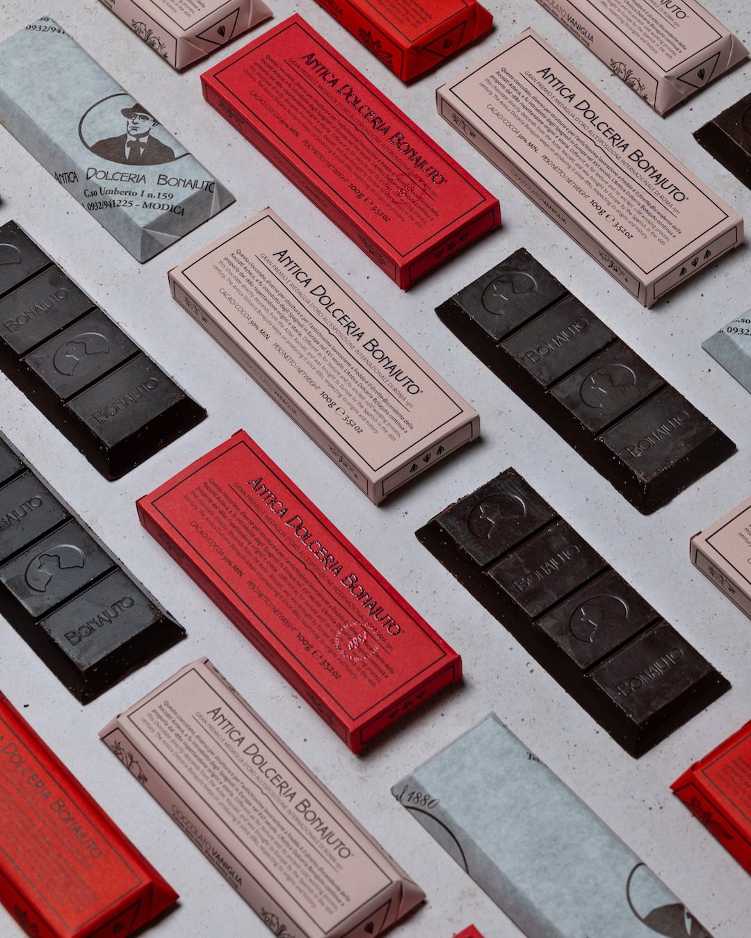 Wrapped Bonajuto chocolate bars in red, pink and grey papers laid out with bare dark bars