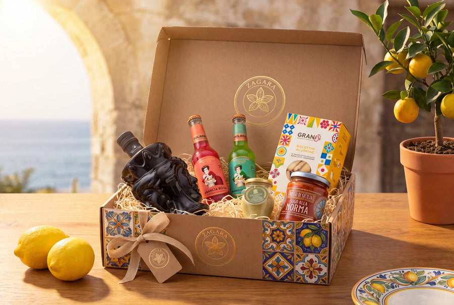 The Sicilian Table gift box open on a table above the sea, packed with bottles, jars and biscuits, lemons beside it