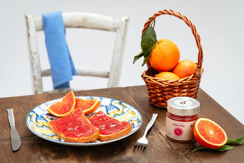 Blood orange marmalade on toast served on a hand-painted Sicilian plate, beside a basket of oranges