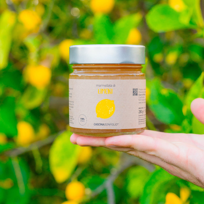 A hand holding a jar of Sicilian lemon marmalade among the fruit of a lemon tree