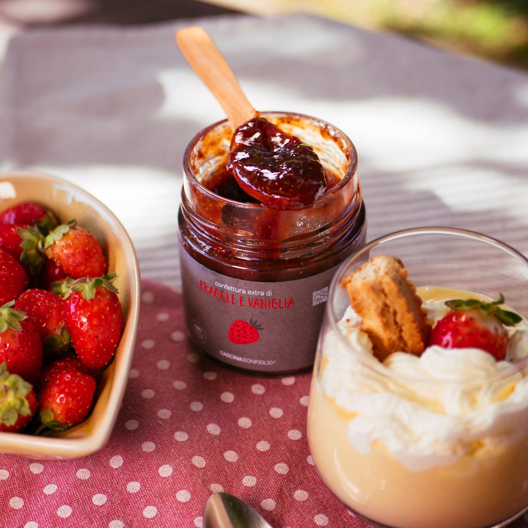 An open jar of strawberry and vanilla preserve with fresh strawberries and a cream dessert