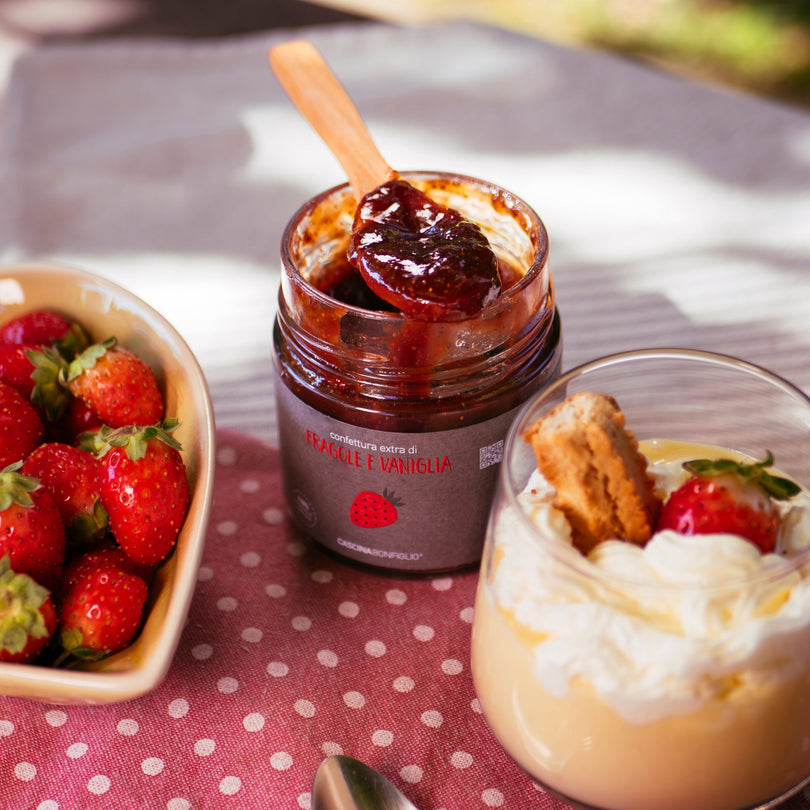 An open jar of strawberry and vanilla preserve with fresh strawberries and a cream dessert