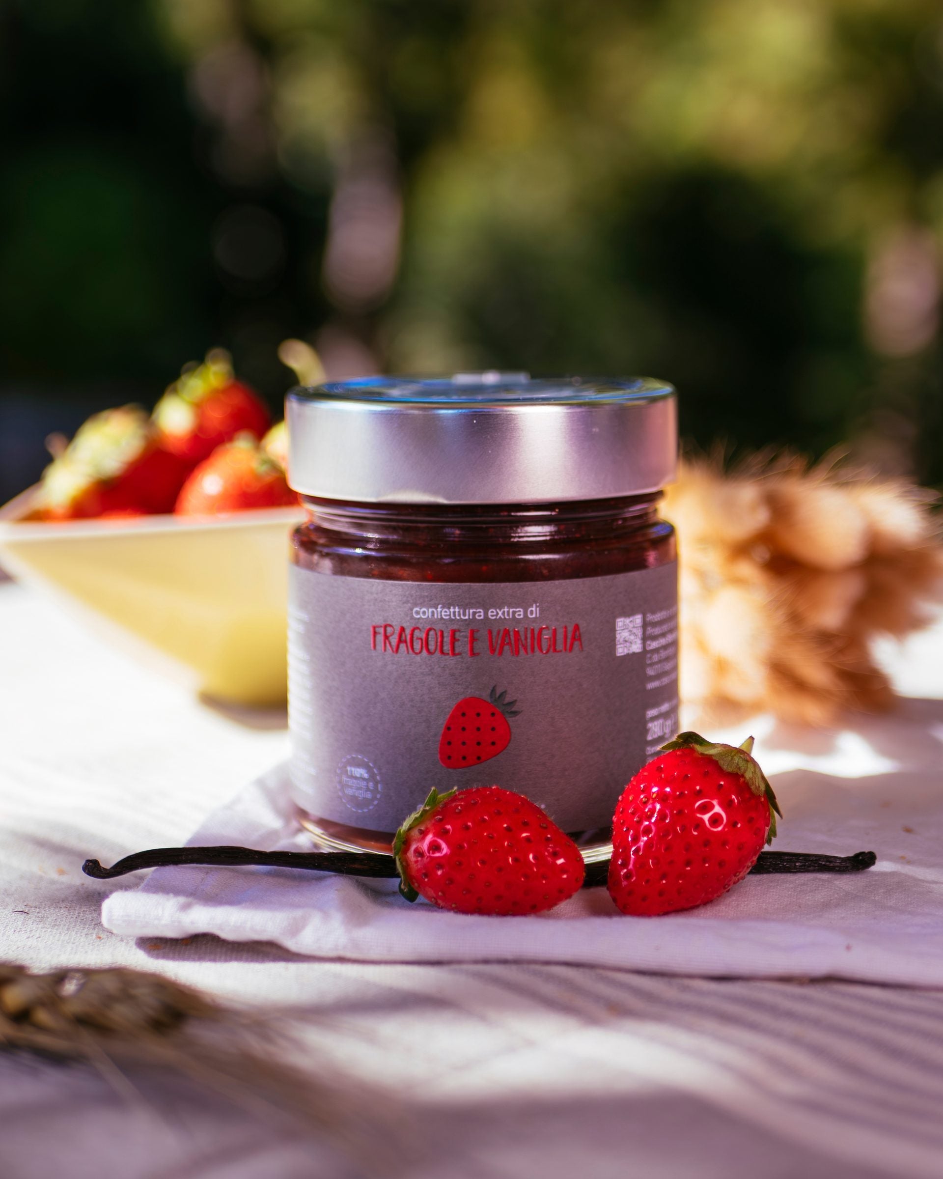 A jar of strawberry and vanilla preserve on linen, with fresh strawberries and vanilla pods
