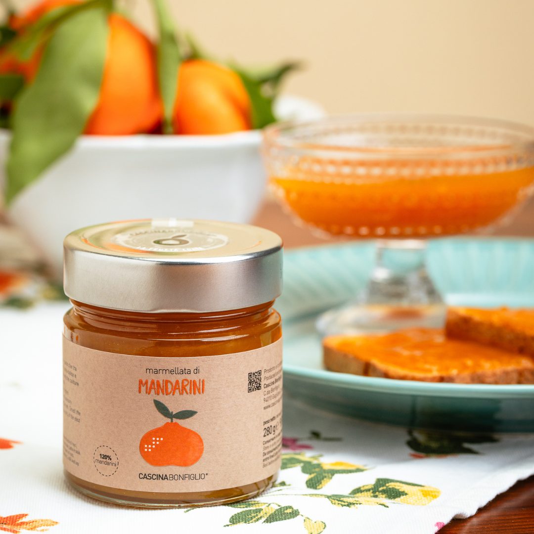 A jar of mandarin marmalade beside fresh mandarins and marmalade on toast