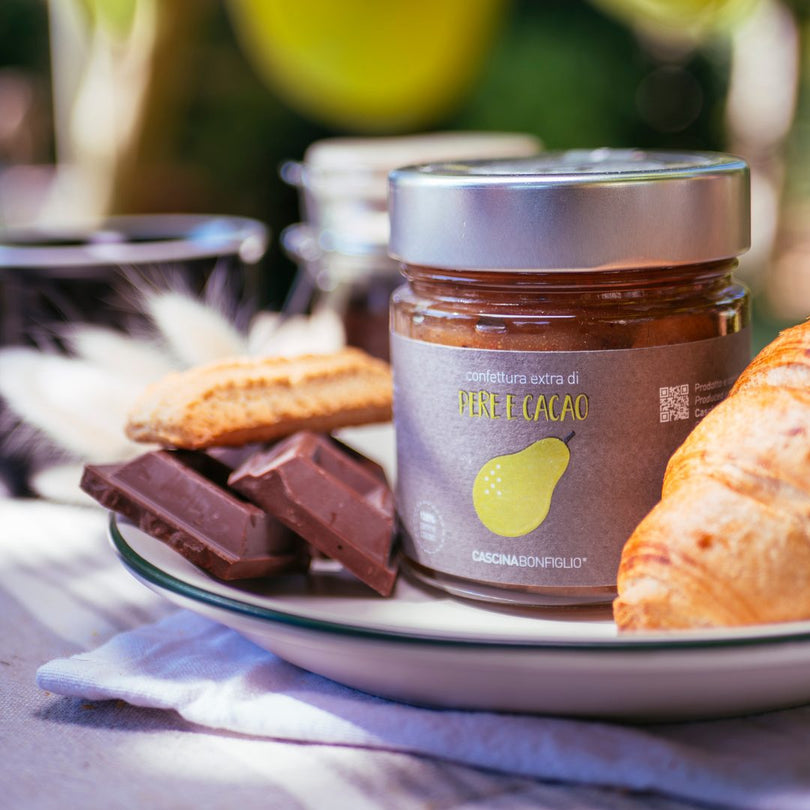 A jar of pear and cocoa preserve with dark chocolate, biscuits and a croissant