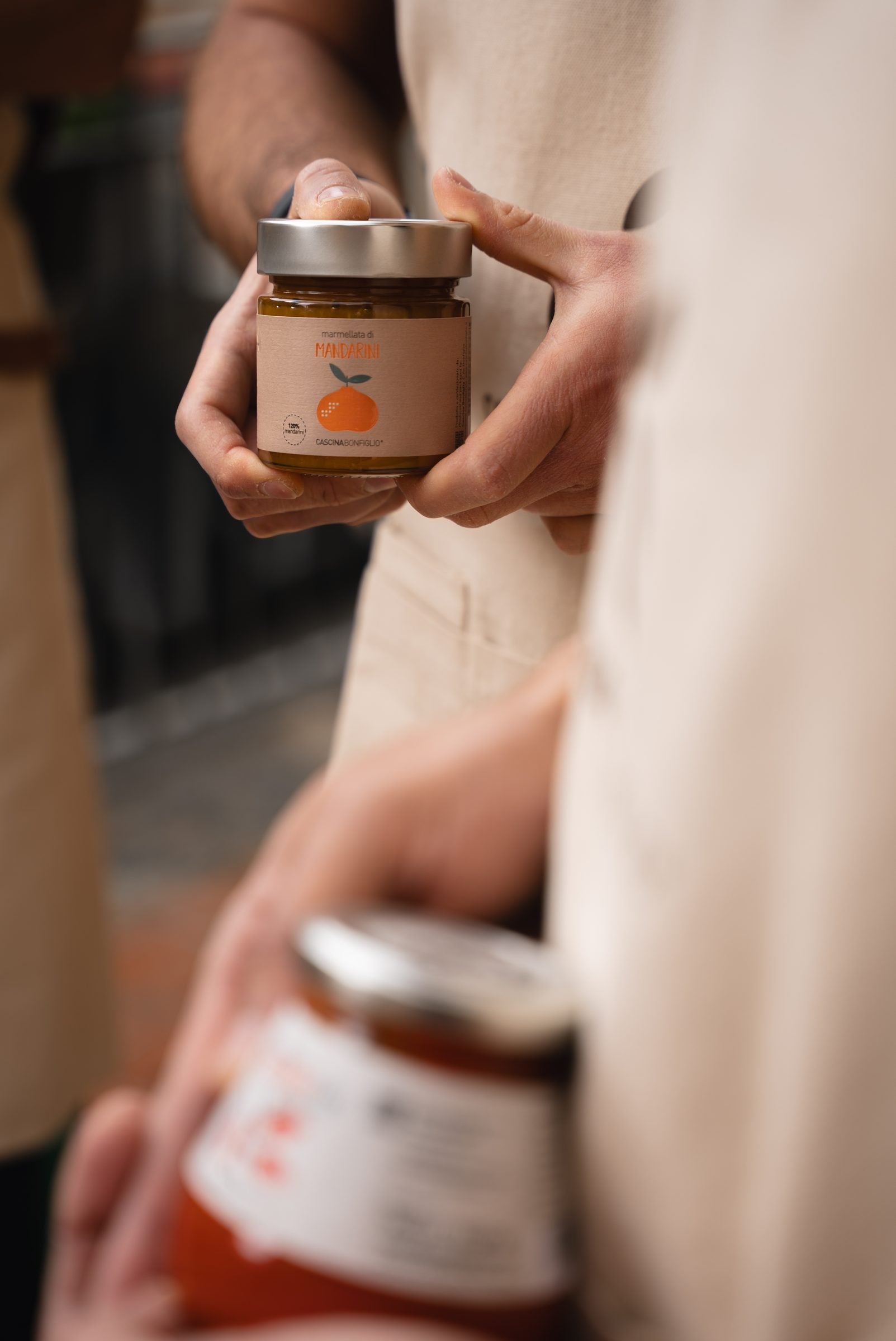 Hands in a Cascina Bonfiglio apron holding a jar of mandarin marmalade