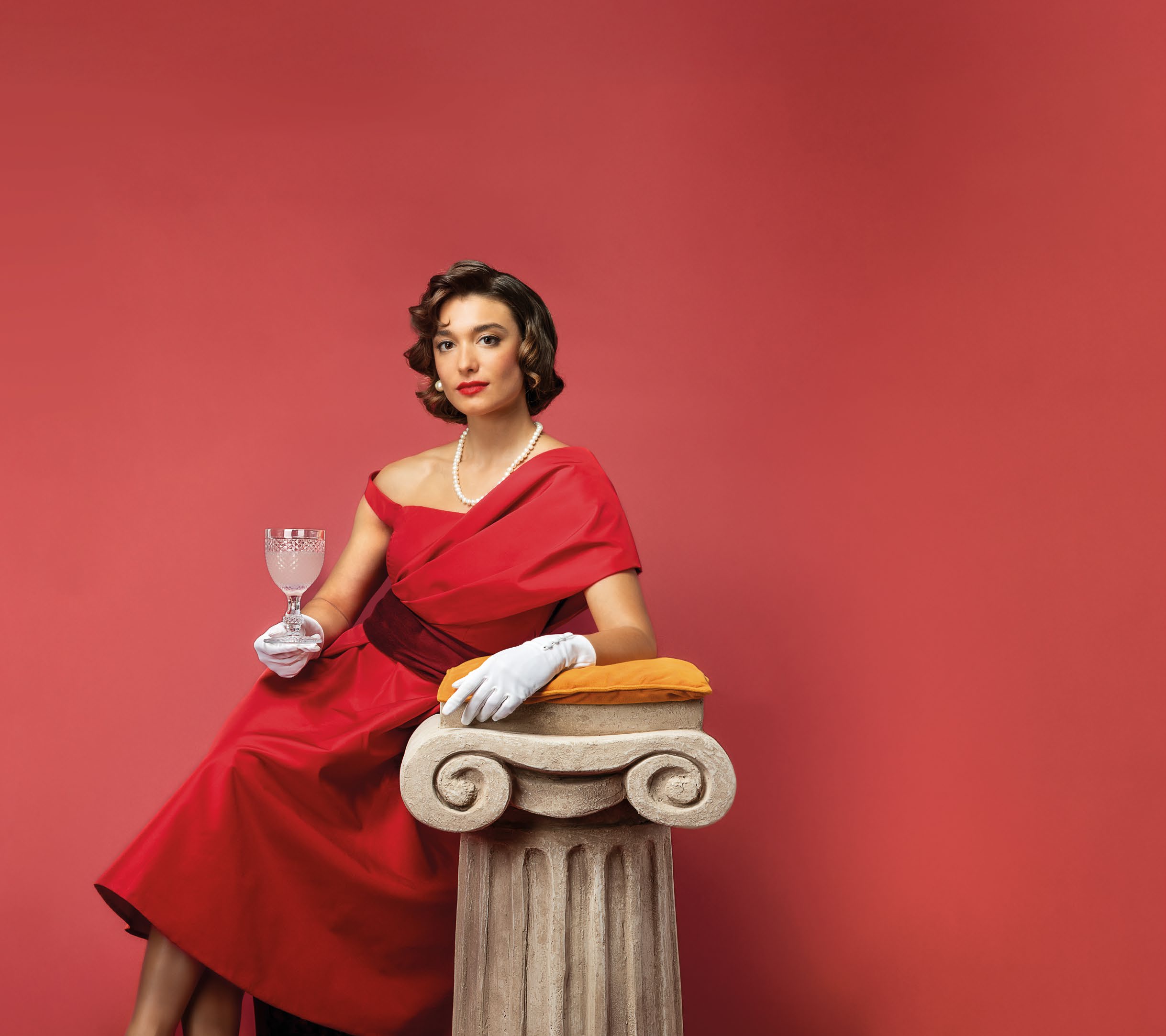 A woman in a red dress and gloves beside a stone column, from Polara's 2025 brochure