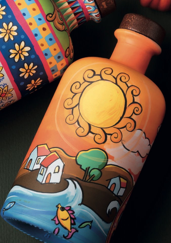 Two decorated olive oil bottles lying on a dark green ground, one with flowers and checks, one orange with a sun, houses and the sea