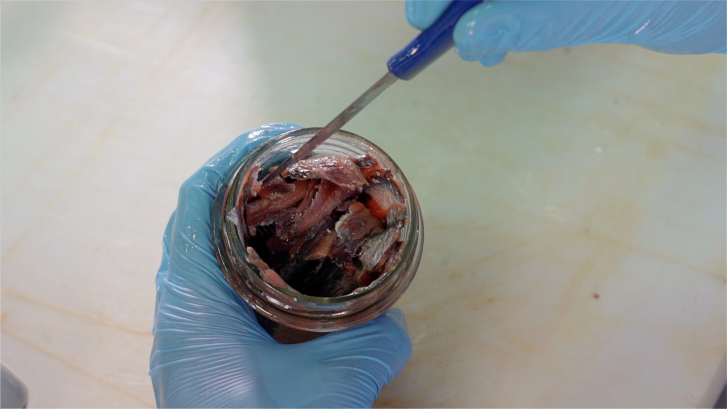 Anchovy fillets being laid one by one into a glass jar by hand