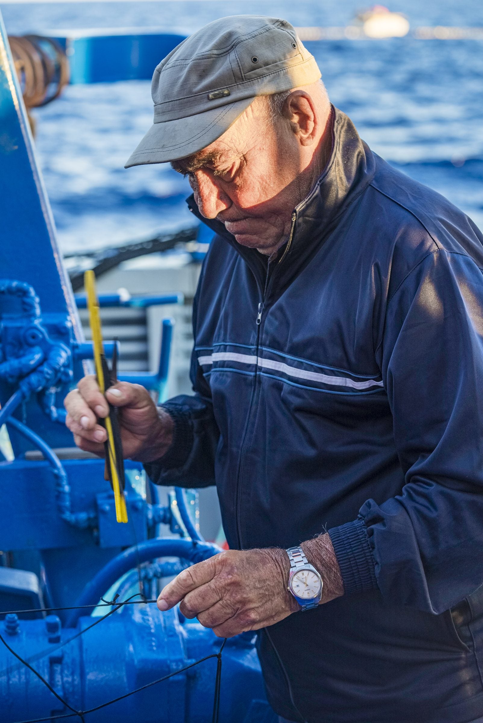 Captain Pippo Testa at work on deck, in a navy jacket and cap, with the sea behind him