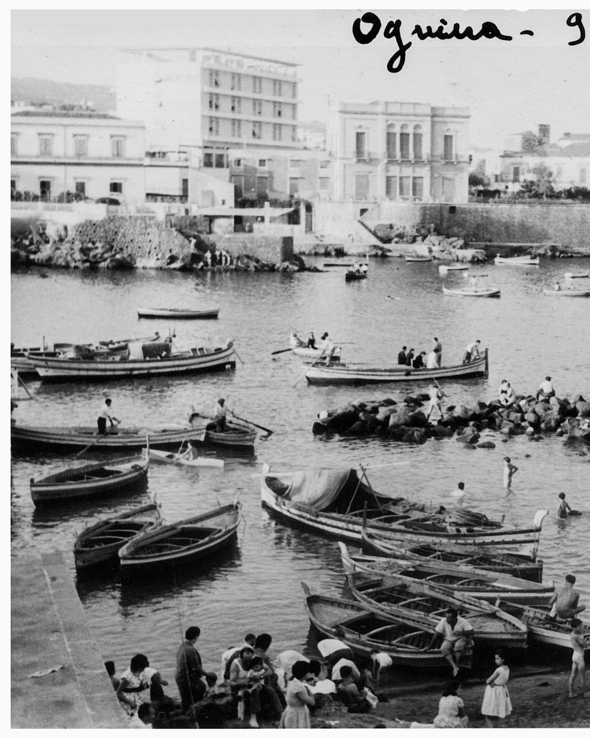 Black-and-white photograph of the small harbour of Ognina, Catania, in 1959, with wooden fishing boats pulled up on the shore