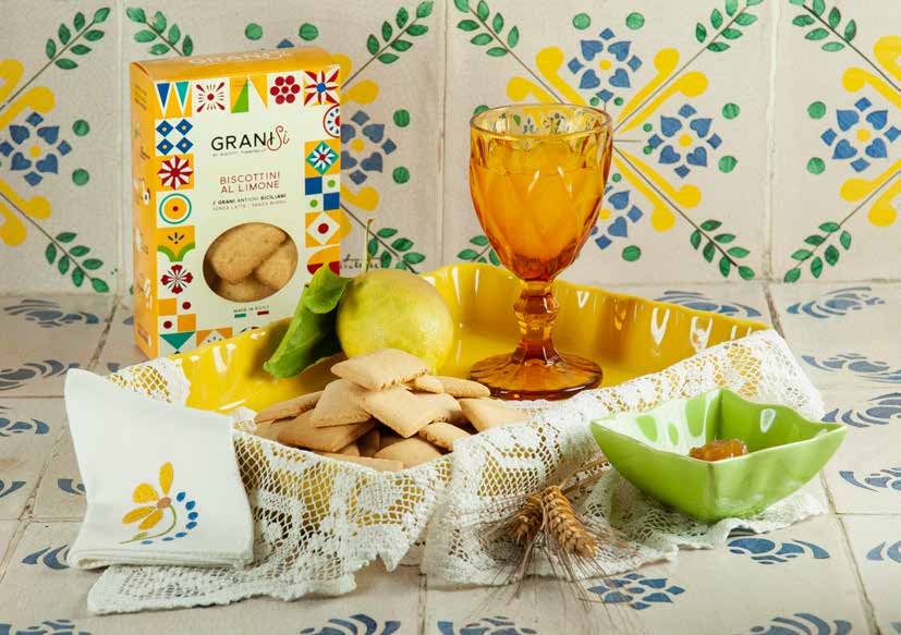 A box of lemon biscuits, the biscuits in a lace-lined basket, a lemon and an amber glass on painted tiles