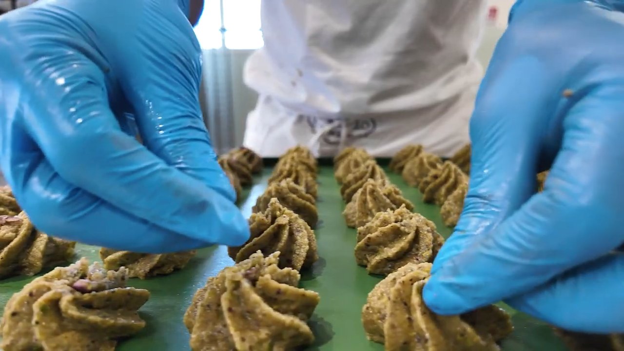 Hands in blue gloves shaping pistachio pastries on a green tray